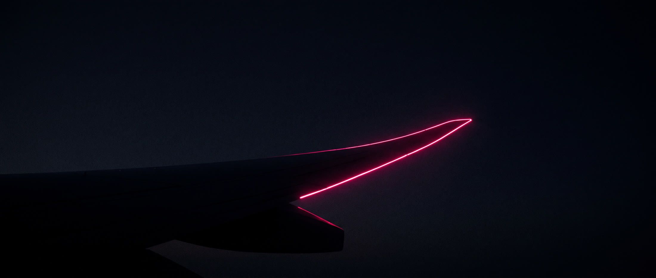 An aircraft wing at night, its trailing edge lit in magenta